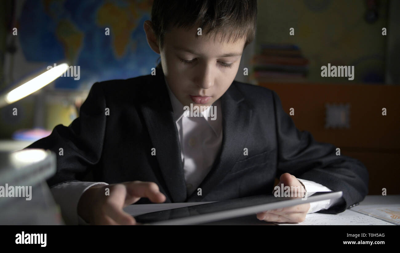 boy in jacket using tablet, doing homework at home, playing at the game Stock Photo