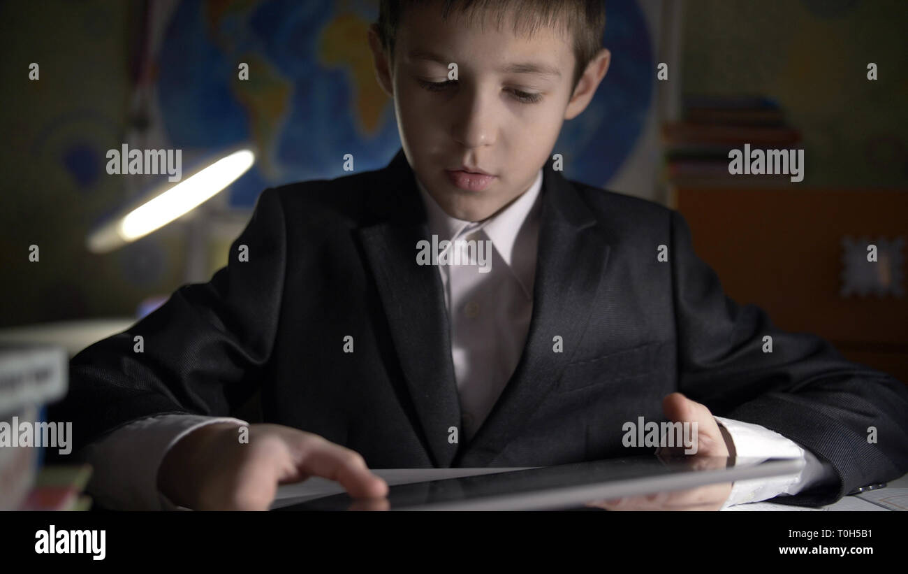 boy in jacket using tablet, doing homework at home, playing at the game Stock Photo