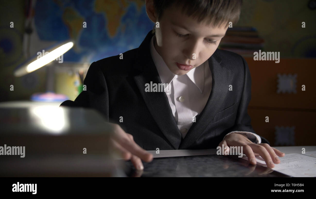 boy in jacket using tablet, doing homework at home, playing at the game Stock Photo