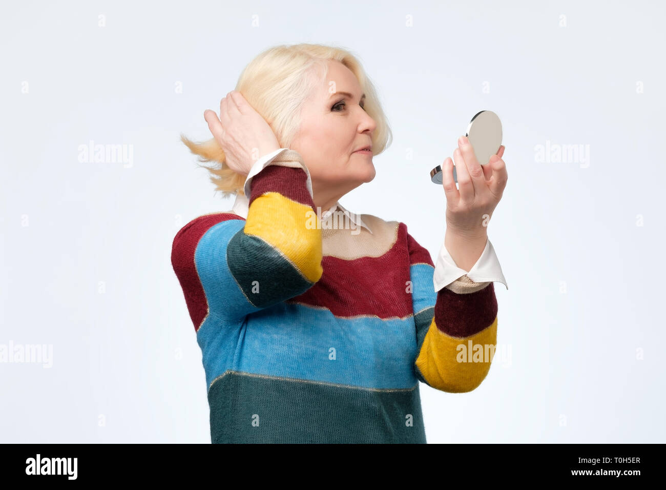 Smiling senior blond woman with mirror over white background Stock Photo