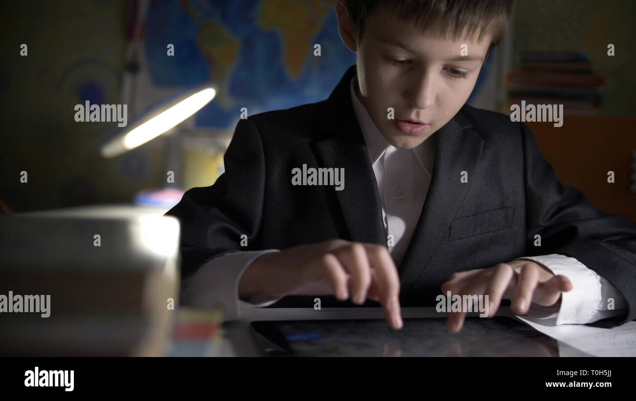 boy in jacket using tablet, doing homework at home, playing at the game Stock Photo