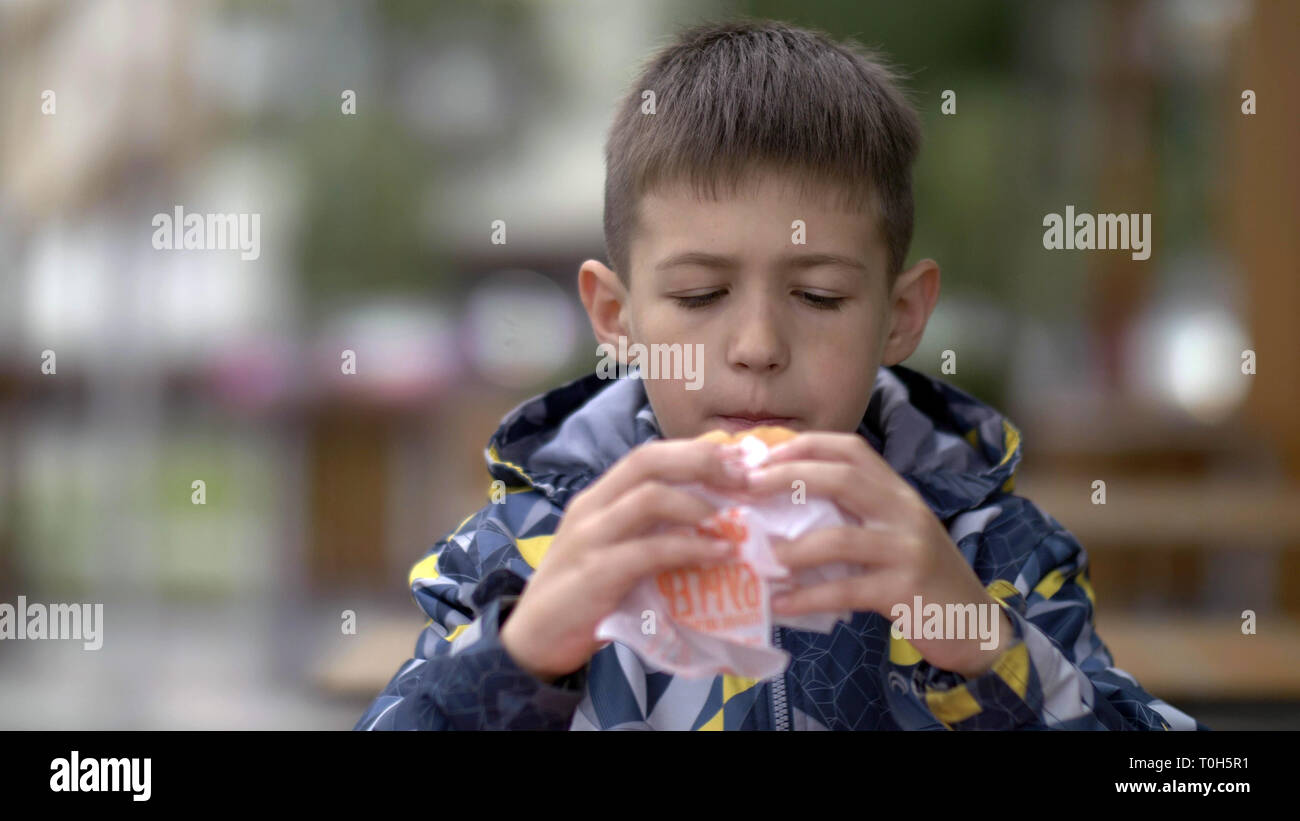 serious young teenager eating burger sitting in cafe in city Stock Photo