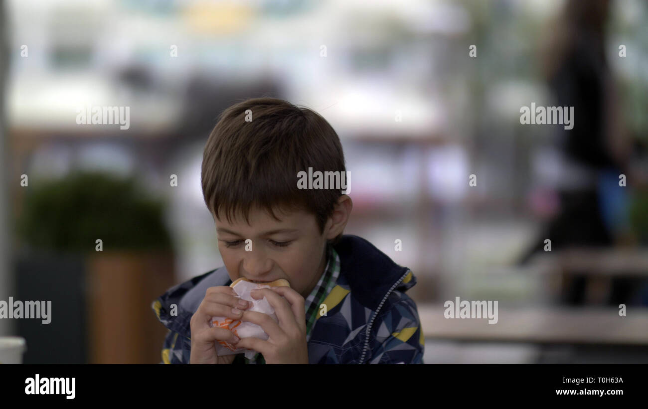 serious young teenager eating burger sitting in cafe in city Stock Photo