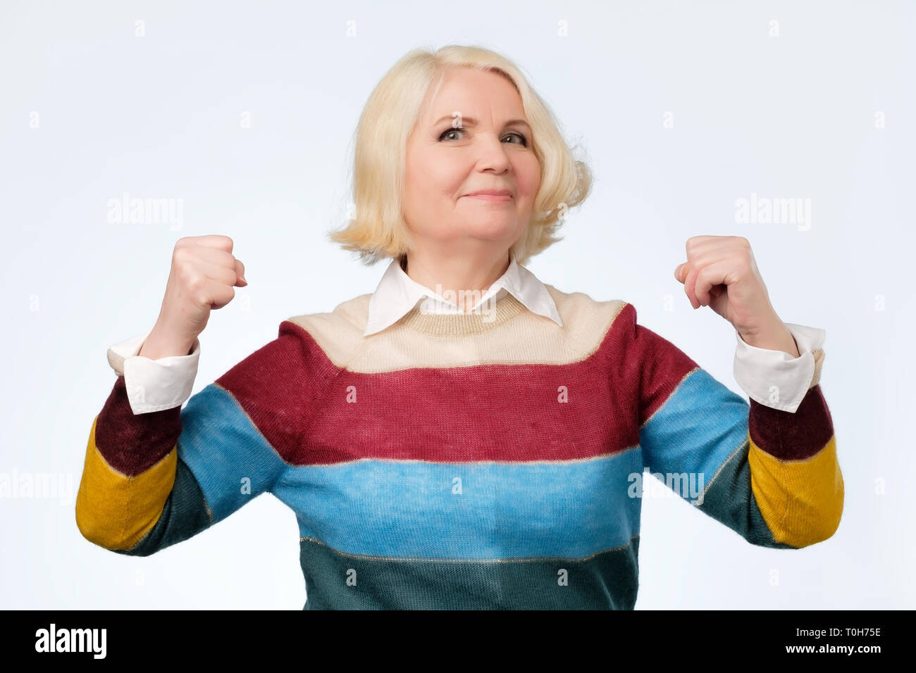 Elderly happy senior woman being proud of herself showing her muscles Stock Photo