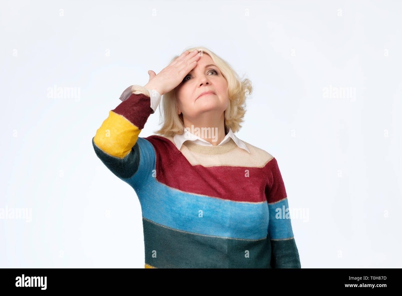 Senior blonde woman surprised with hand on head for mistake, remember error Stock Photo