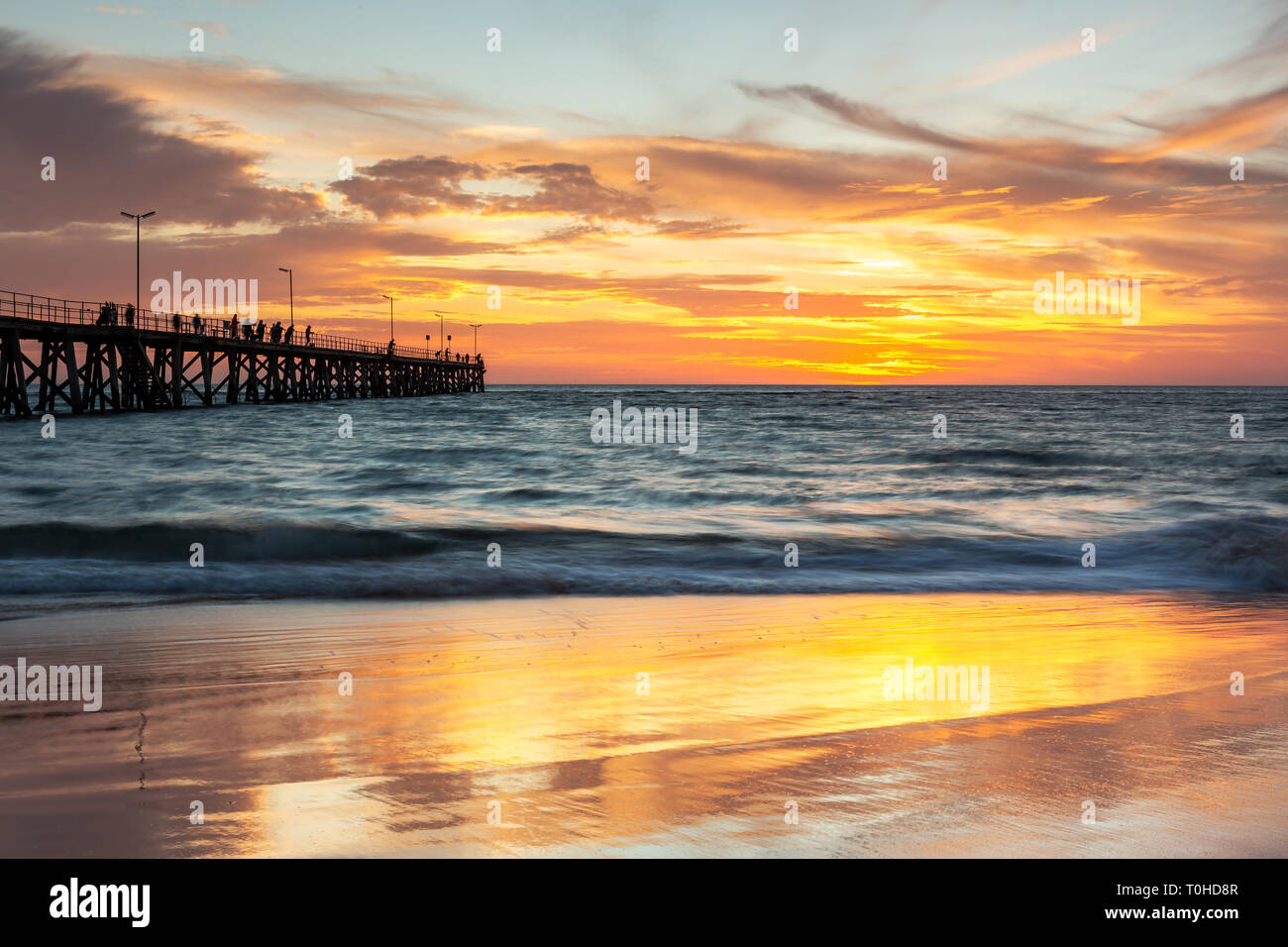 A beautiful sunset at Port Noarlunga with the jetty and sunset reflections on the sand at Port Noarlunga South Australia Stock Photo