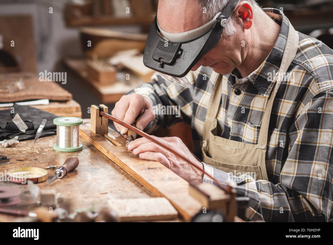 Violin maker inside a rustic workshop is working on a bow with precision Stock Photo