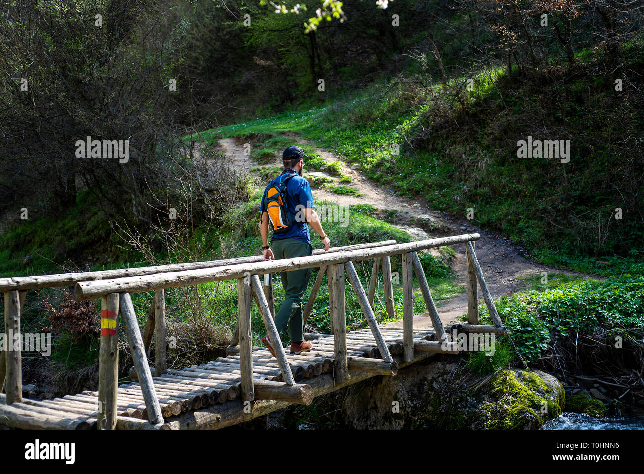 Hiker crossing the wooden bridge over small river Stock Photo