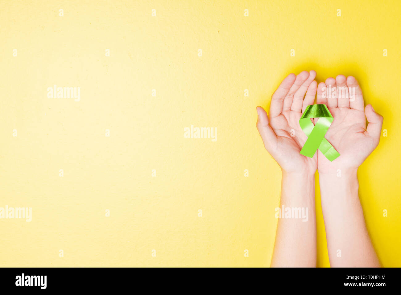 Human hands showing green ribbon over yellow color background. Health ...