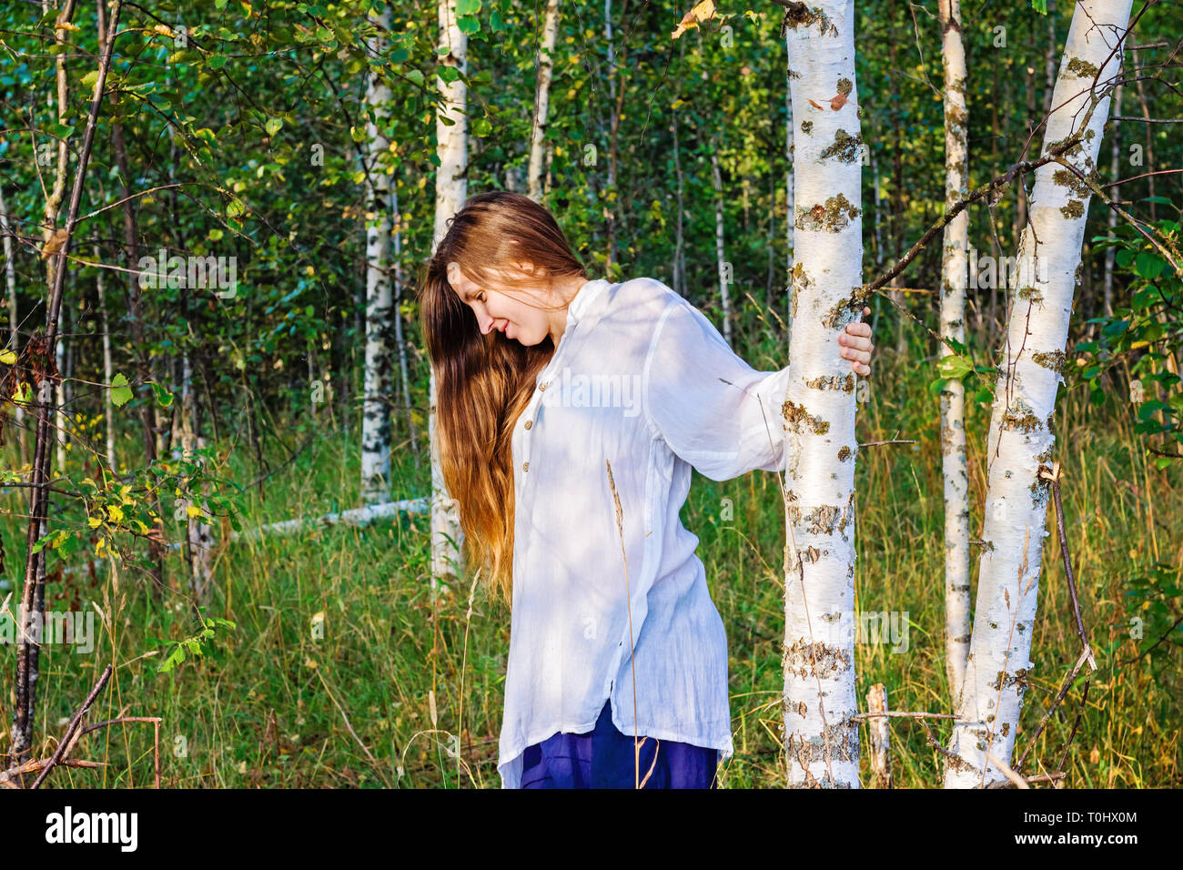 The young girl the blonde smiles near a birch in the wood Stock Photo ...
