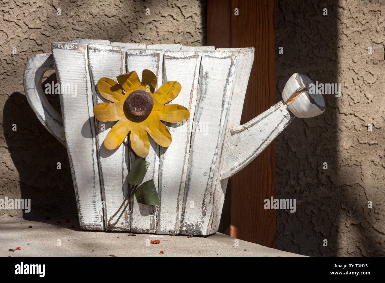 Wood watering can planter with colourful gold flower on side on step of house (day before spring) in Inglewood district of Calgary, Alberta, Canada Stock Photo