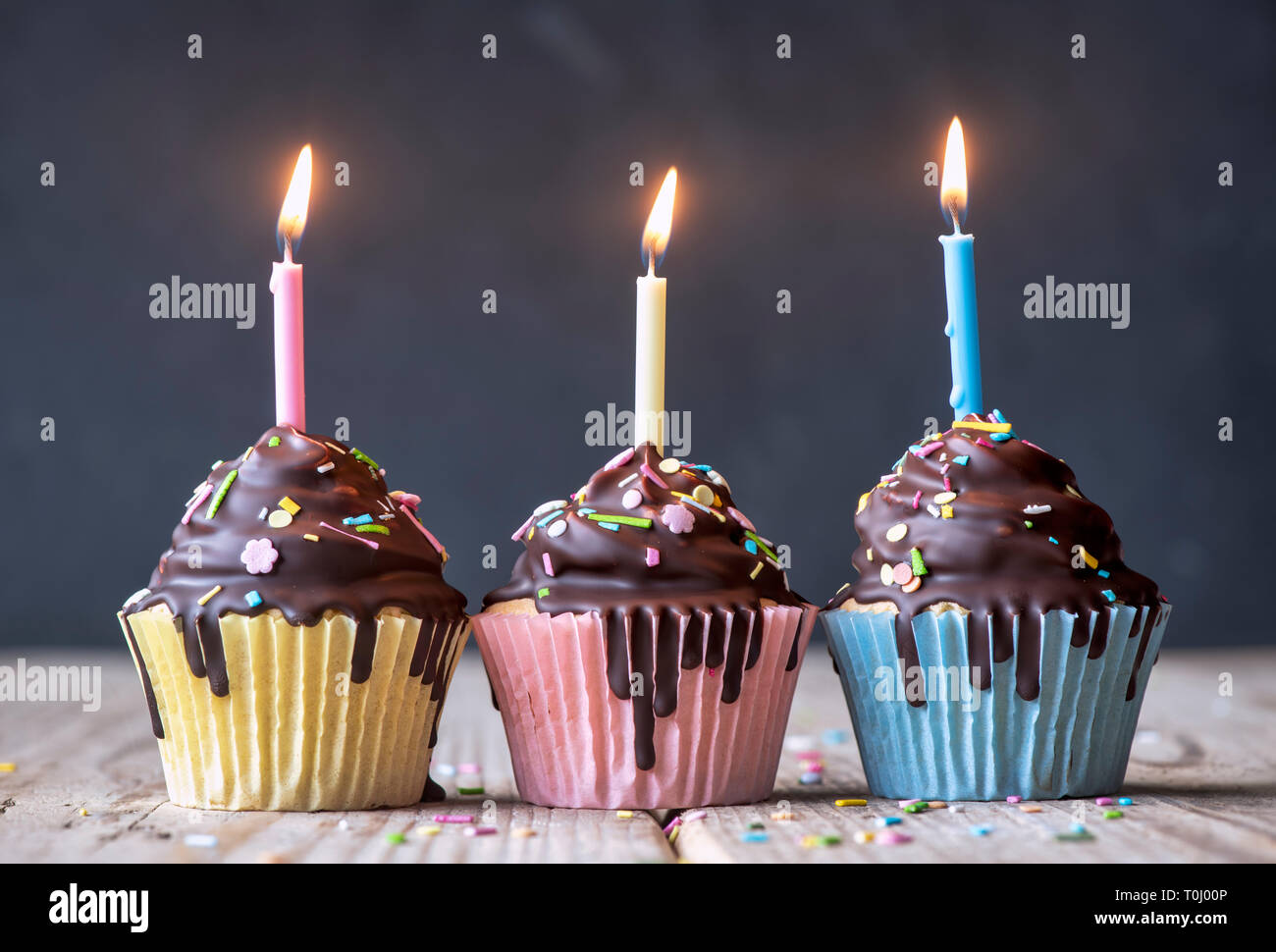 Birthday cupcakes with candles. Vanilla cupcakes with a meringue frosting and dark chocolate shell Stock Photo