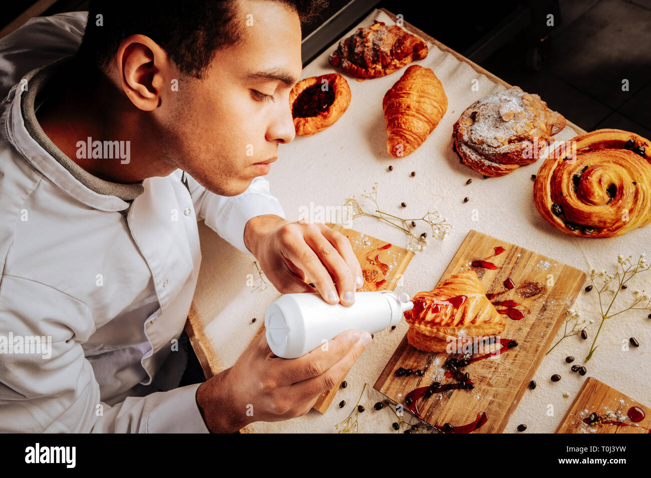 Diligent young baker feeling joyful while decorating pastry Stock Photo