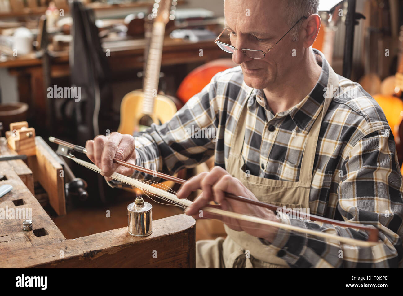 Instrument maker skillfully heating the hair of a violin bow Stock Photo