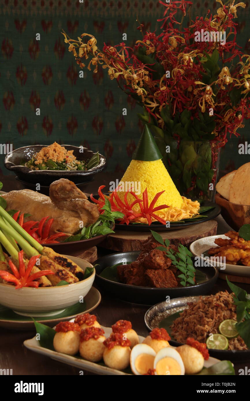 Nasi Tumpeng Nusantara. Festive and grand Indonesian Rijsttafel of yellow rice in cone shape with seven side dishes from regional cuisines. Stock Photo