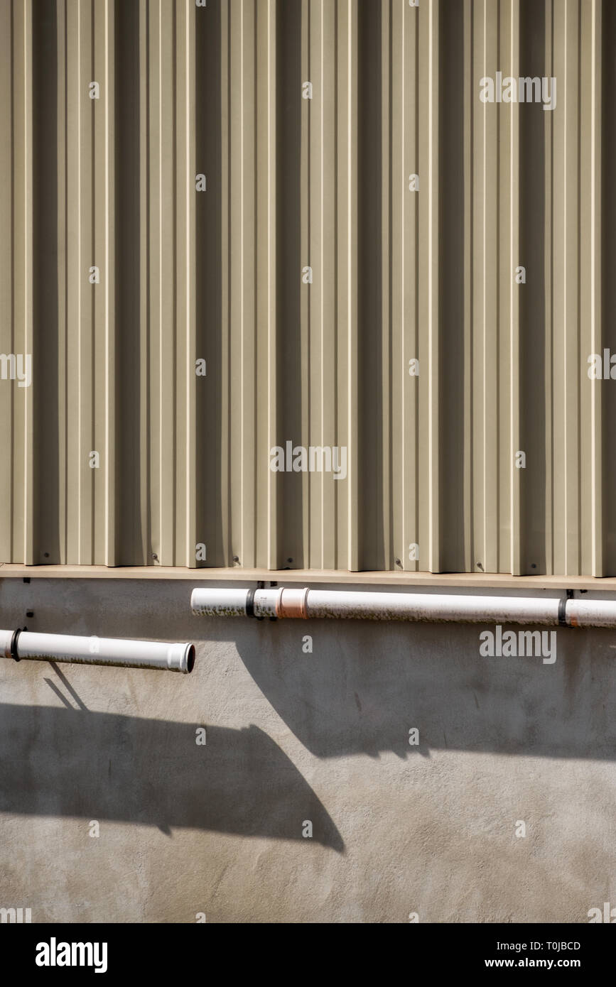 A commercial building wall and disconnected gutter with long shadows Stock Photo