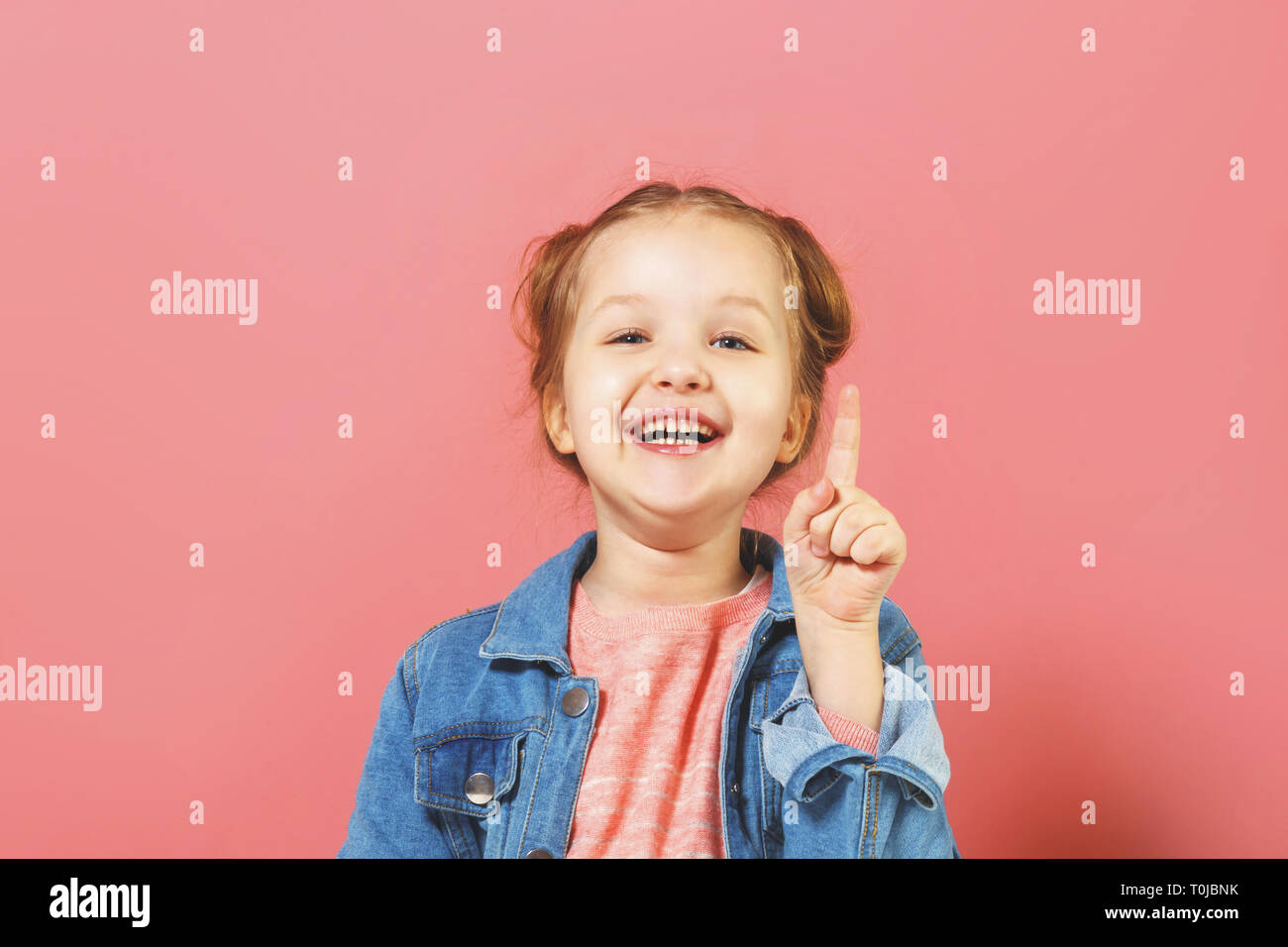 Funny little girl points her finger up. The concept of education. Pink background. Stock Photo