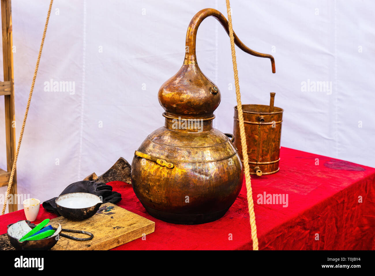 A medieval chemical vessel made of copper. Metal bucket, earthenware on a table covered with red cloth. White canvas in the background Stock Photo