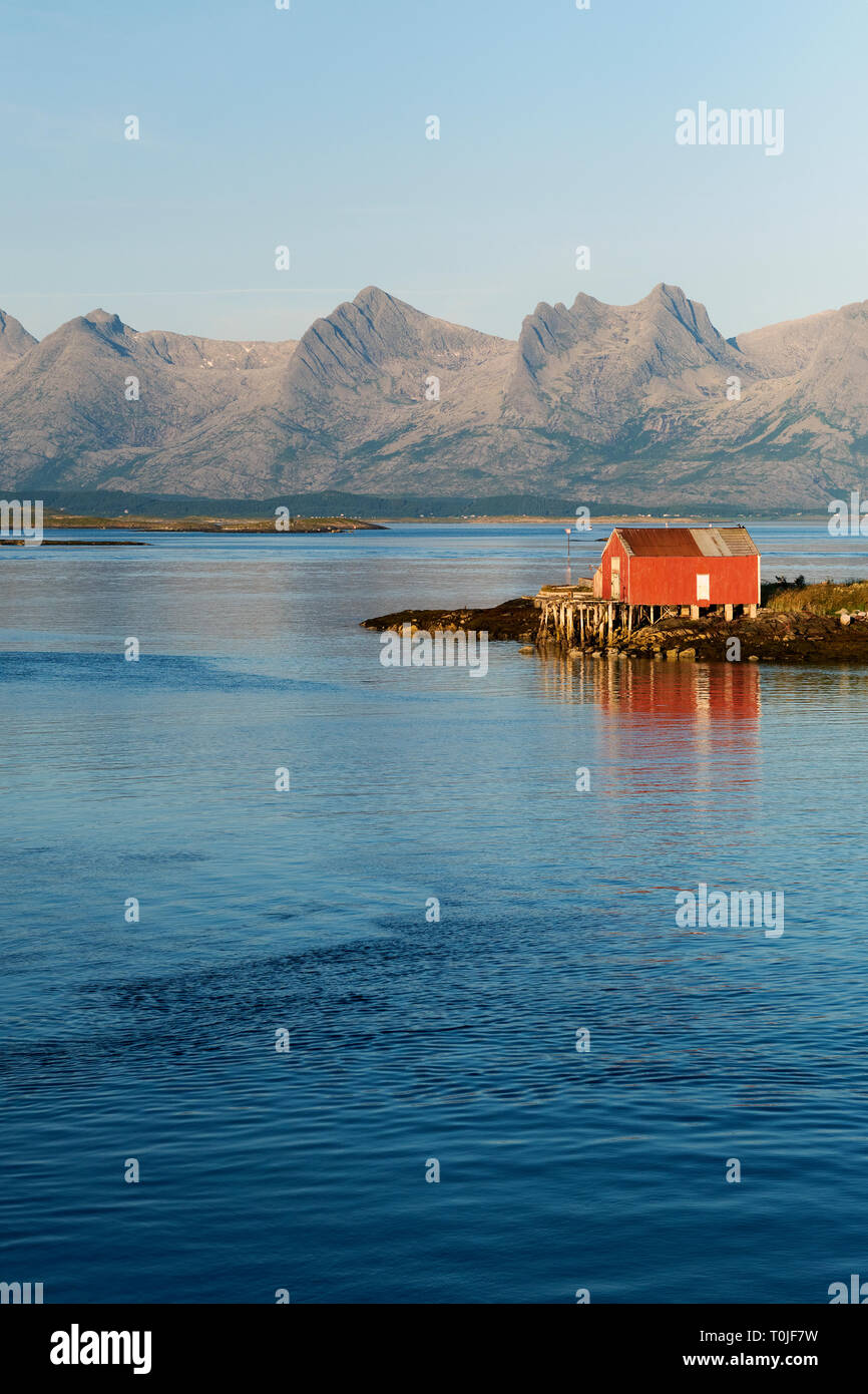 A red Rorbuer house and coastline and De syv søstre / The Seven Sisters mountain range on the island of Alsten in Alstahaug in Nordland county, Norway Stock Photo
