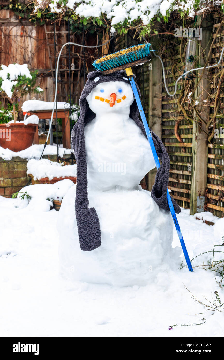 A snowman wearing a scarf and holding a blue household broom in a North London back garden Stock Photo