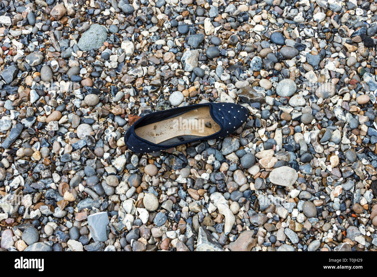 A woman's fancy shoe washed up on the stony shore of the River Thames in London, UK Stock Photo