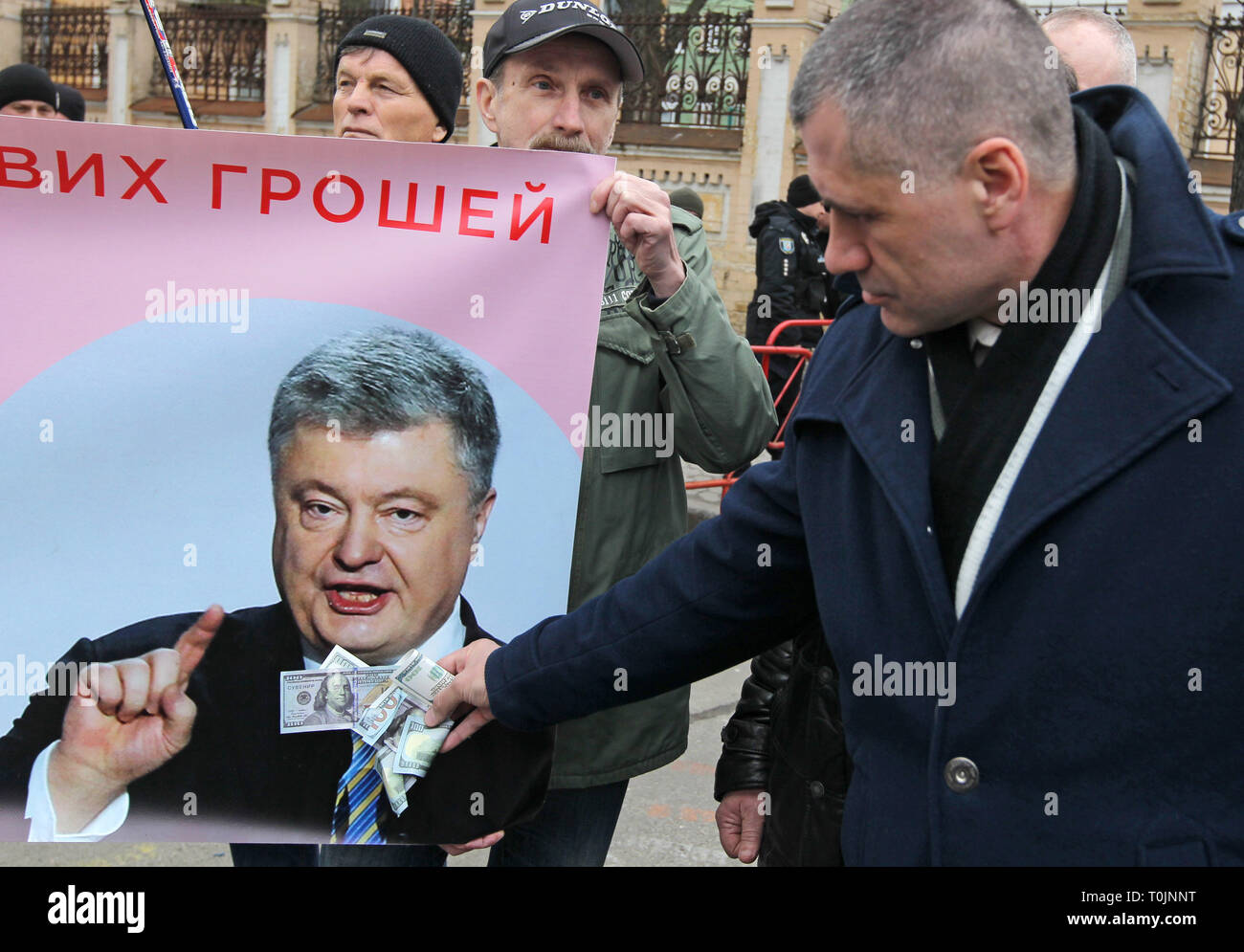 Kiev, Kiev, Ukraine. 20th Mar, 2019. An activist of the ''Movement of New Force party, of former Georgian President Mikhael Saakashvili, is seen holding fake dollar bills in front of a banner with a photo of Ukrainian President Petro Poroshenko outside the Presidential office during the protest.The activists protest against alleged corruption in the country's defence industry, and demand an investigation and arrests of the top figures in an alleged military corruption scandal, which they were accused of profiting from the sales of state defence companies at inflated prices of smuggled Russi Stock Photo
