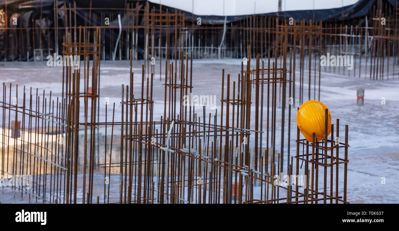 Reinforced concrete, under construction. Columns steel bars reinforcement and yellow hardhats in a construction site, closeup view. Stock Photo