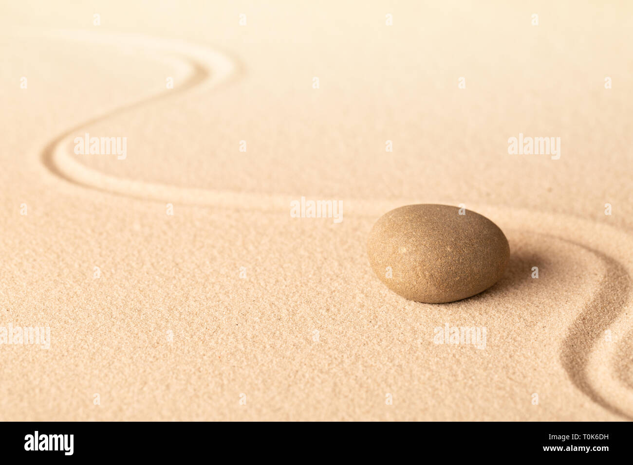 Concentration trough focus on a zen meditation stone. Round rock in sand texture background. Concept for yoga or spa welness treatment. Stock Photo