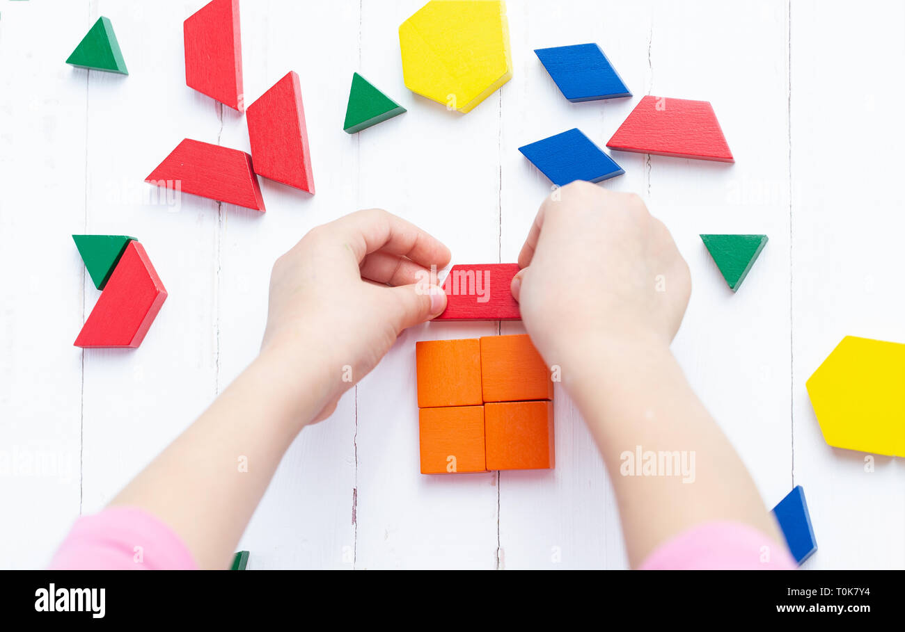 A child plays with colored blocks constructs a model on a light wooden background Stock Photo