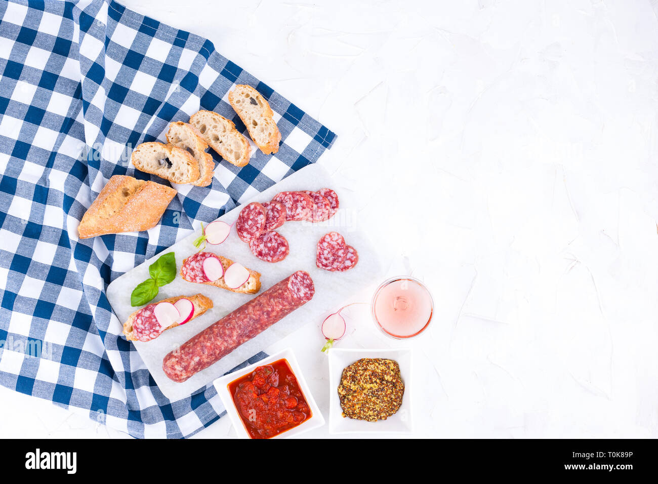 Italian salami on a white board and a stone background, a glass of rose