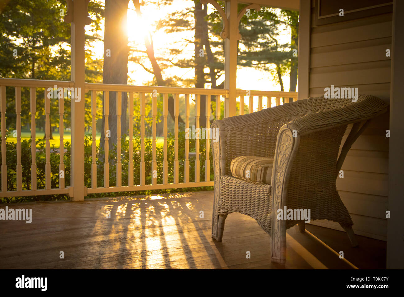 Warm sunny look over an empty comfortable chair and cozy front porch. Stock Photo