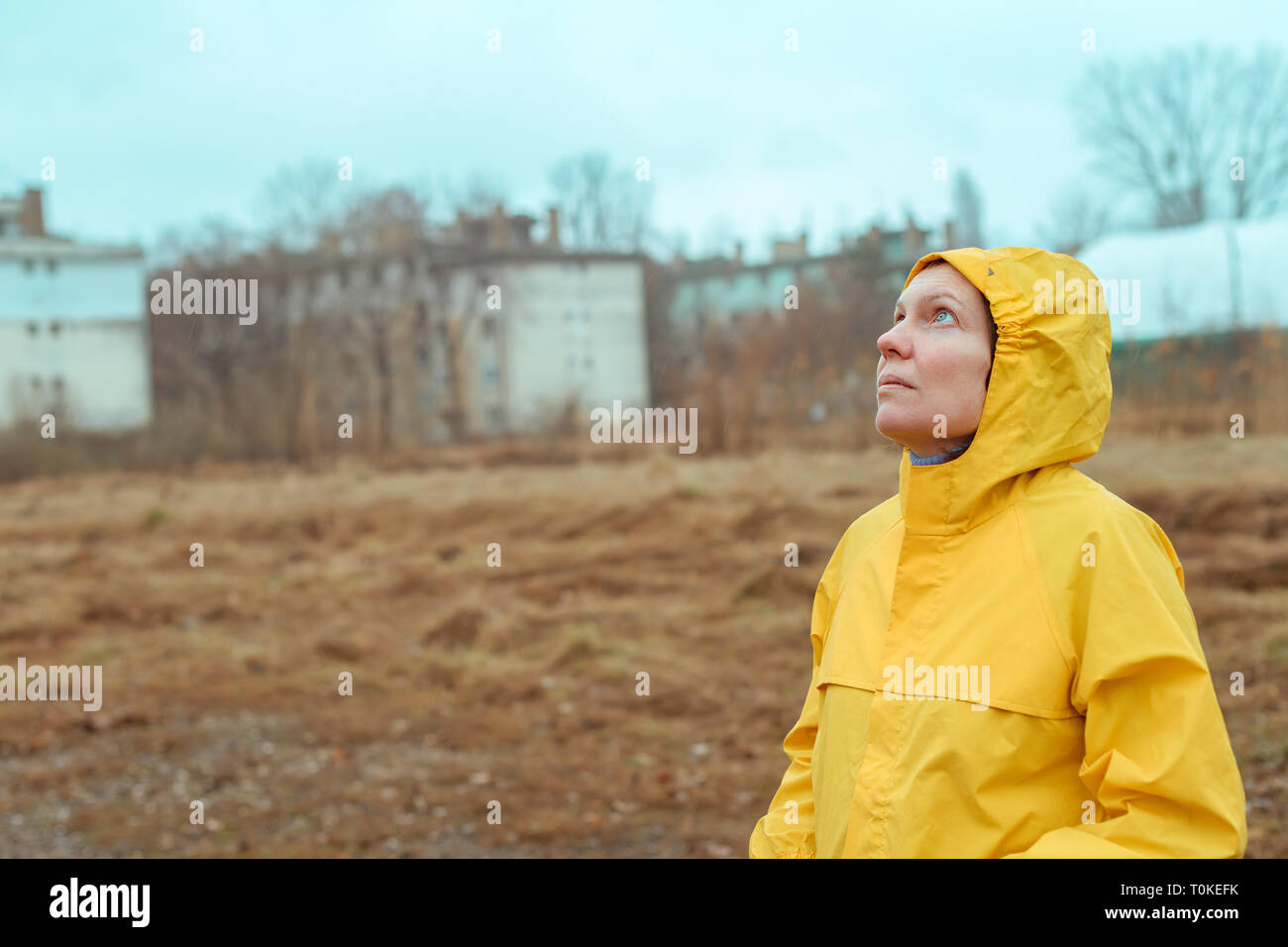 Woman in yellow raincoat looking up at rainy clouds while the raindrops are falling on her face Stock Photo