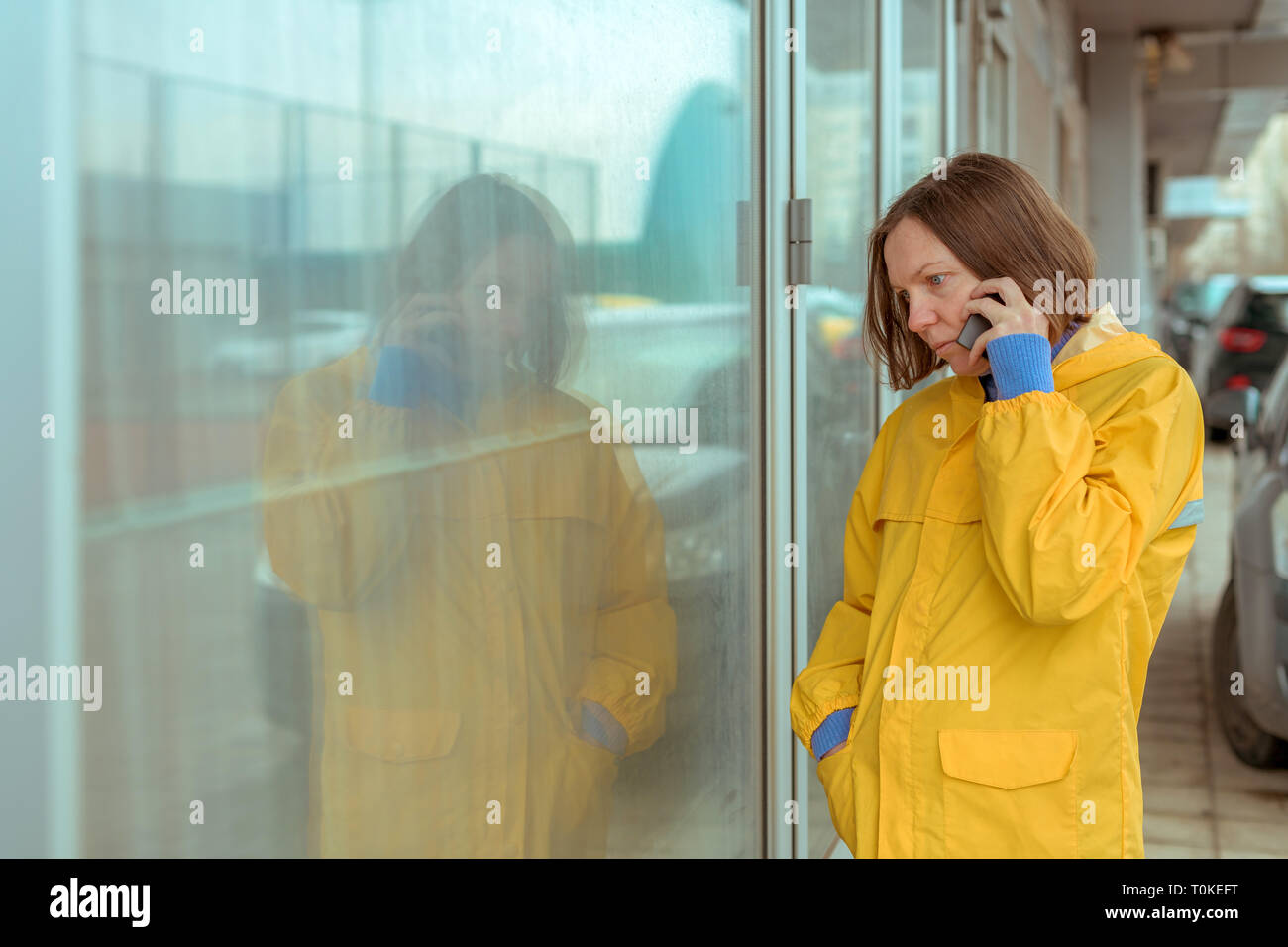 Sad woman in yellow raincoat talking on mobile phone out on the street while it's raining Stock Photo