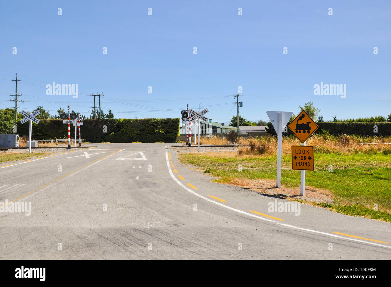 Railway crossing in the Canterbury region of New Zealand. Country crossing without gates or barrier. Look for trains sign. Steam engine graphic Stock Photo