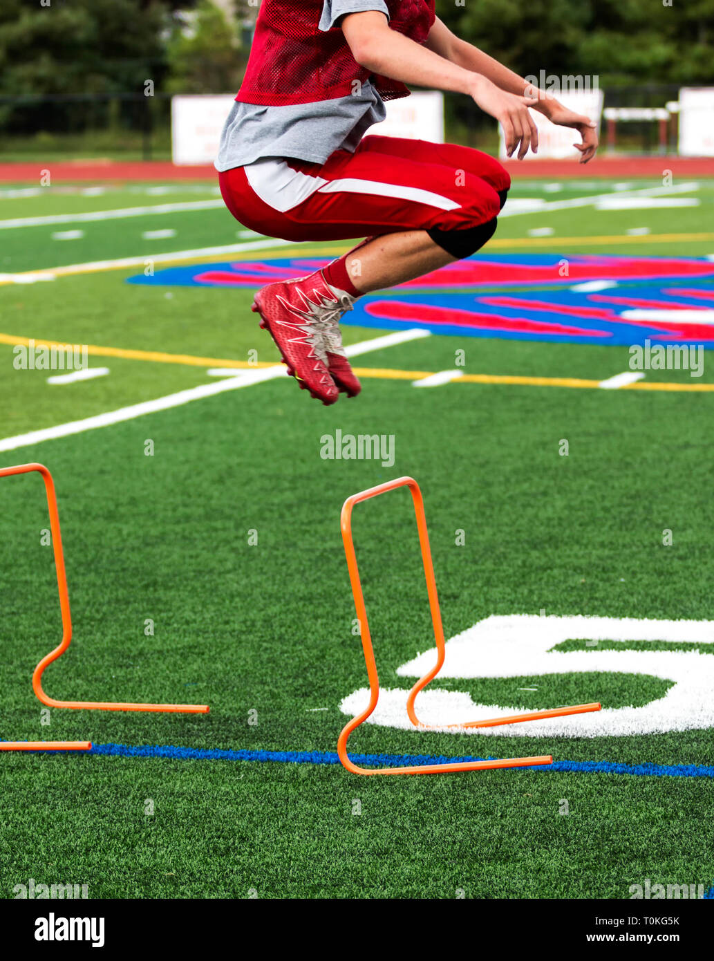 A high school football player jumps over orange hurdles during practice