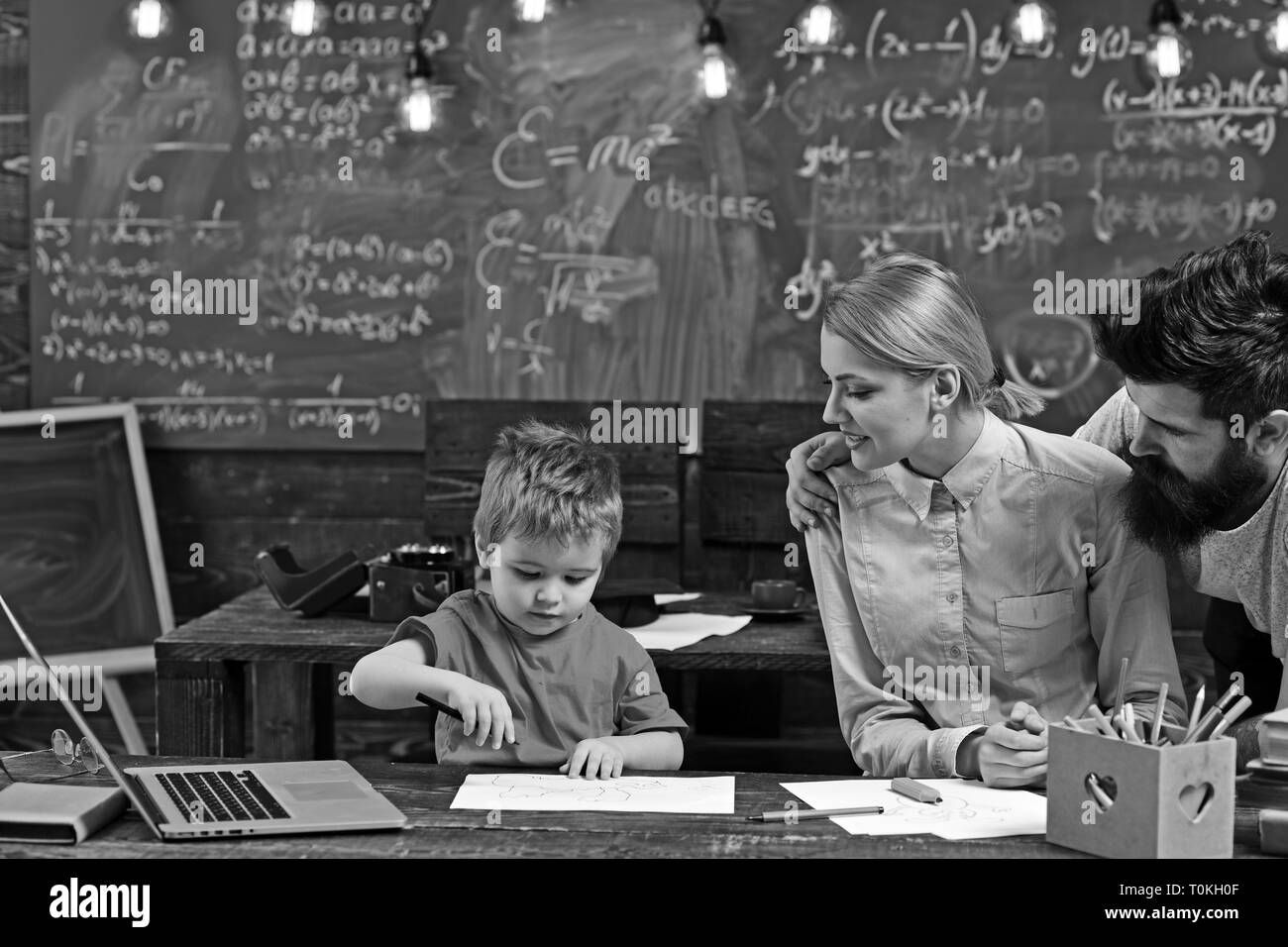 Young parents looking at son coloring in drawing book on desk Stock Photo