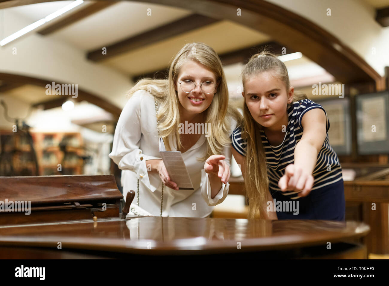 Portrait of woman with girl holding guidebook, pointing to art objects ...