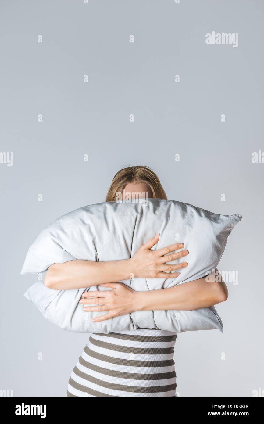 Young woman hugging a gray pillow, hiding her face behind it. Stock Photo