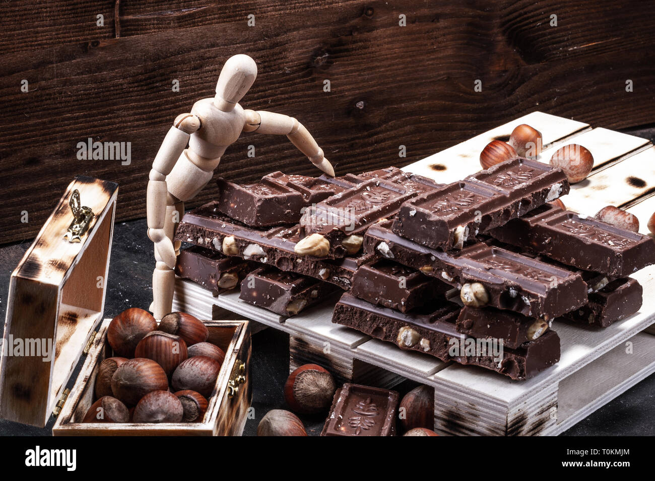 Large amounts of milk chocolate in piles on boards. Hazelnuts in a crate. Stock Photo