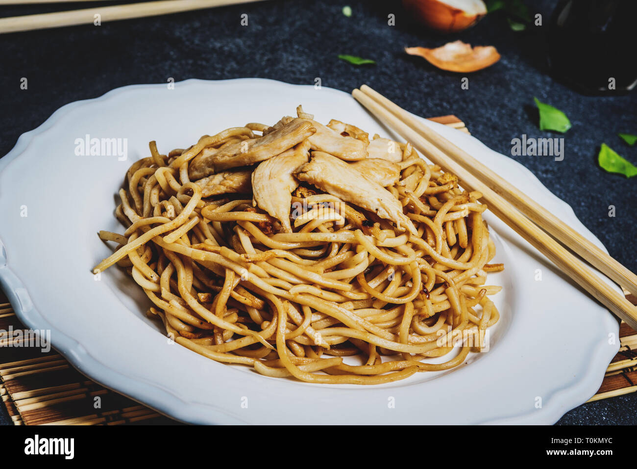 Traditional asian or chines noodles with chicken meat on white plate with chopsticks on dark stone table Stock Photo
