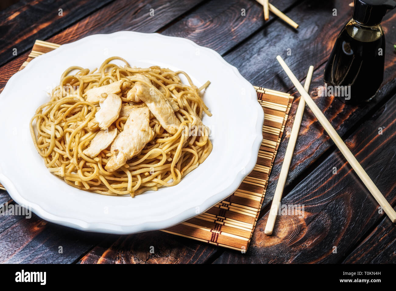 Traditional asian or chines noodles with chicken meat on white plate with chopsticks on wood table Stock Photo