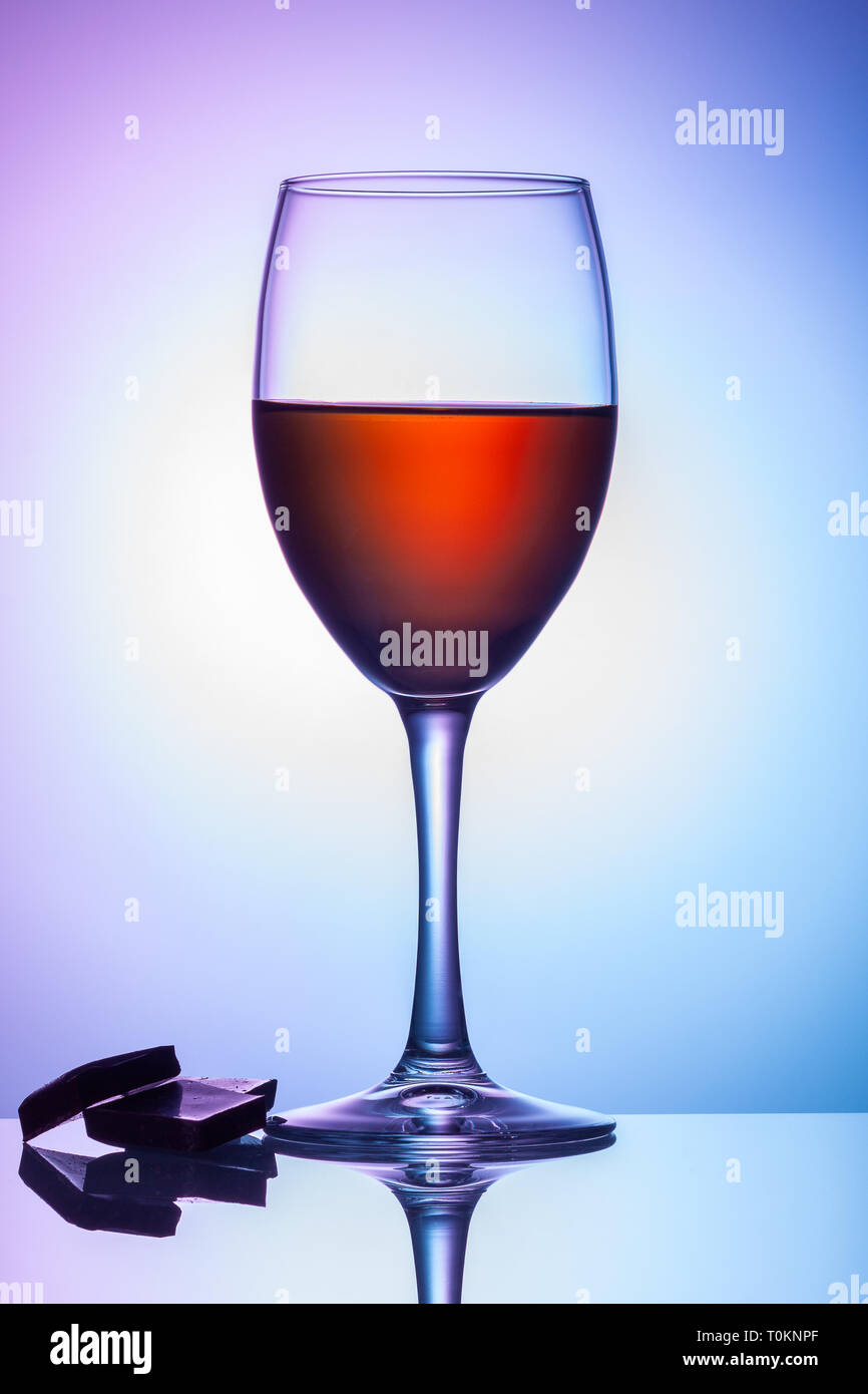 A glass of wine stands on a table against a blue-violet background. Stock Photo