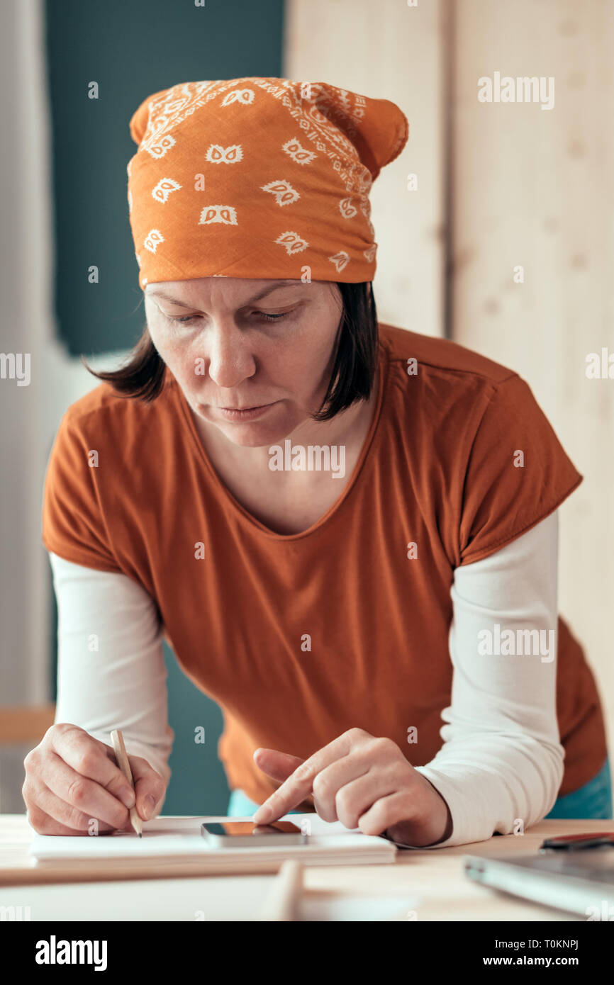 Female carpenter with head kerchief doing financial calculation in carpentry woodwork workshop Stock Photo