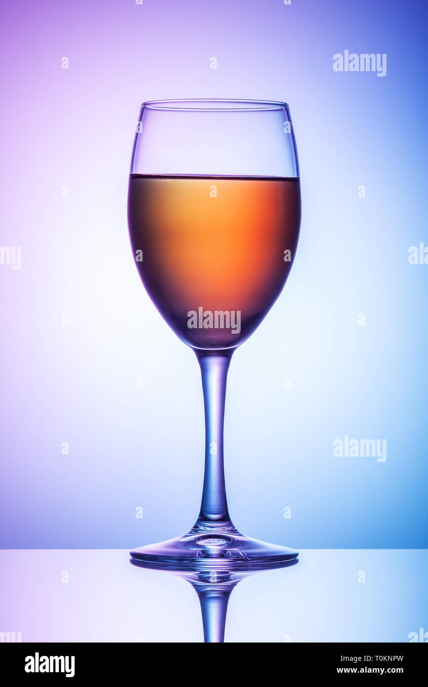 A glass of wine stands on a table against a blue-violet background. Stock Photo