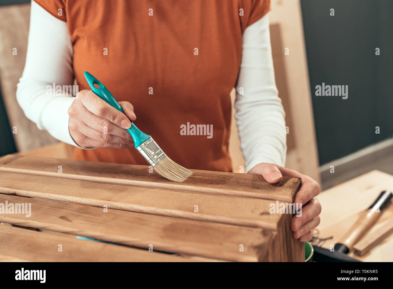 Female carpenter varnishing wooden crate with brush in her small business woodwork workshop Stock Photo