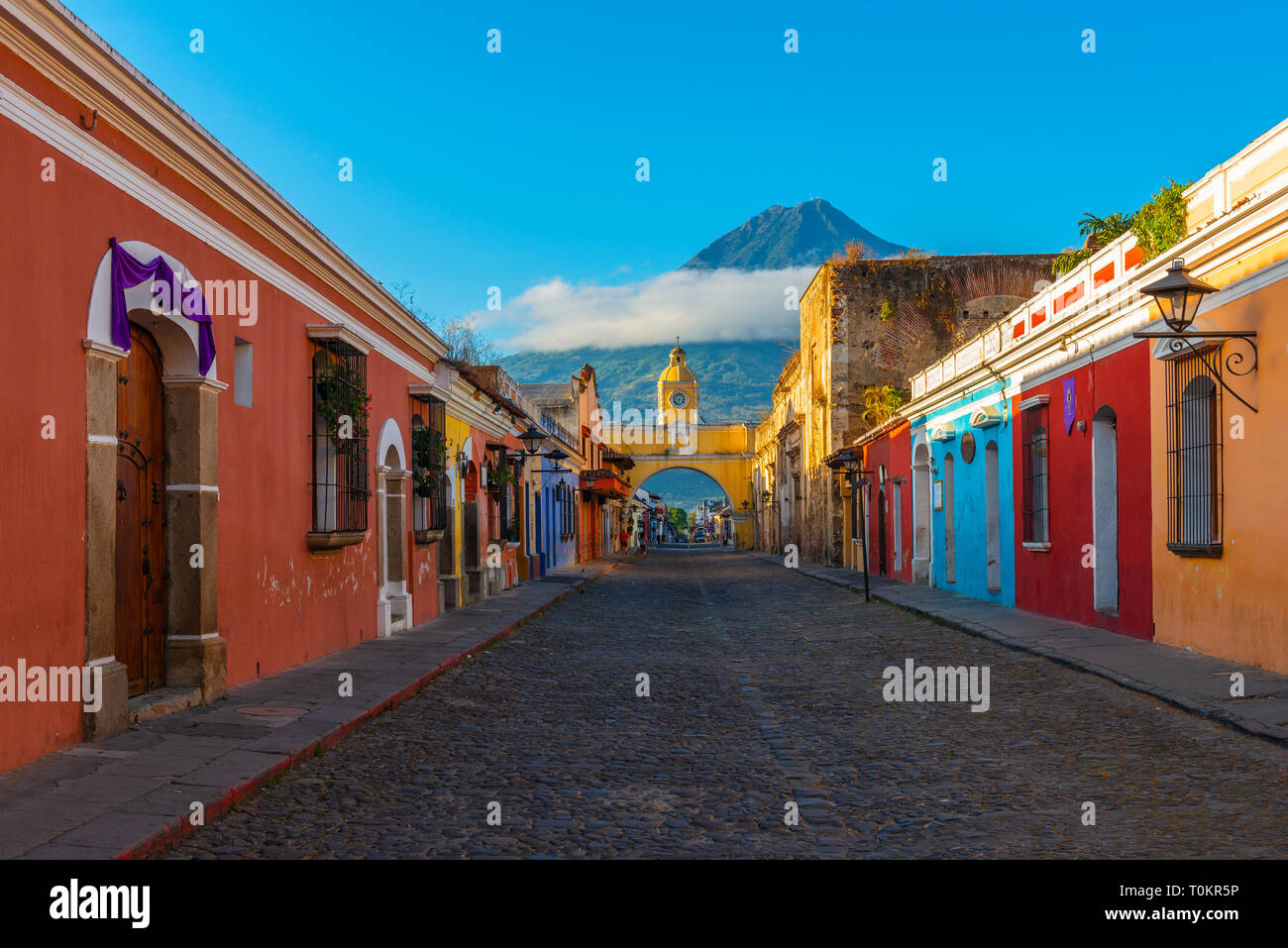 Cityscape of the main street and yellow Santa Catalina arch in the historic city center of Antigua at sunrise with the Agua volcano, Guatemala. Stock Photo