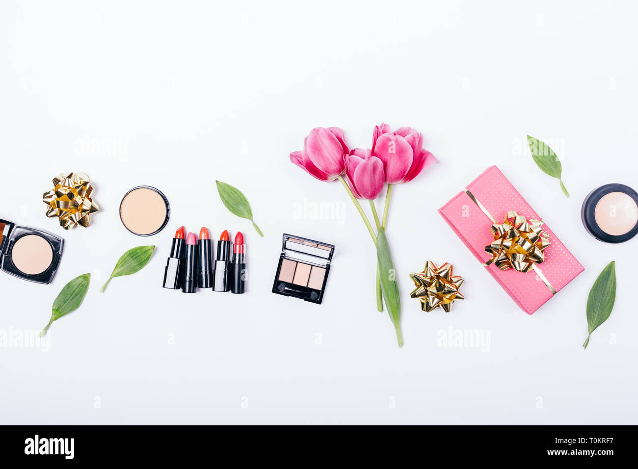 Bouquet of pink tulips near makeup beauty products and gift box on white background, top view. Festive flat lay composition of professional cosmetics: Stock Photo