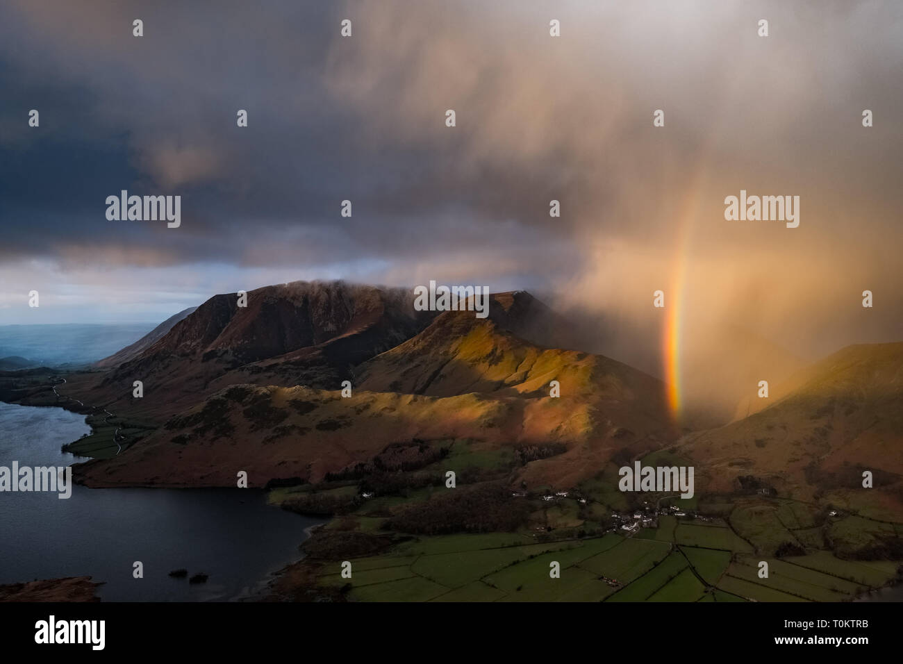 A shower passes over Crummock water, Grasmoor, Rannerdale Knots, Whiteless Pike & Buttermere village, producing a vivid rainbow. Lake District, UK Stock Photo