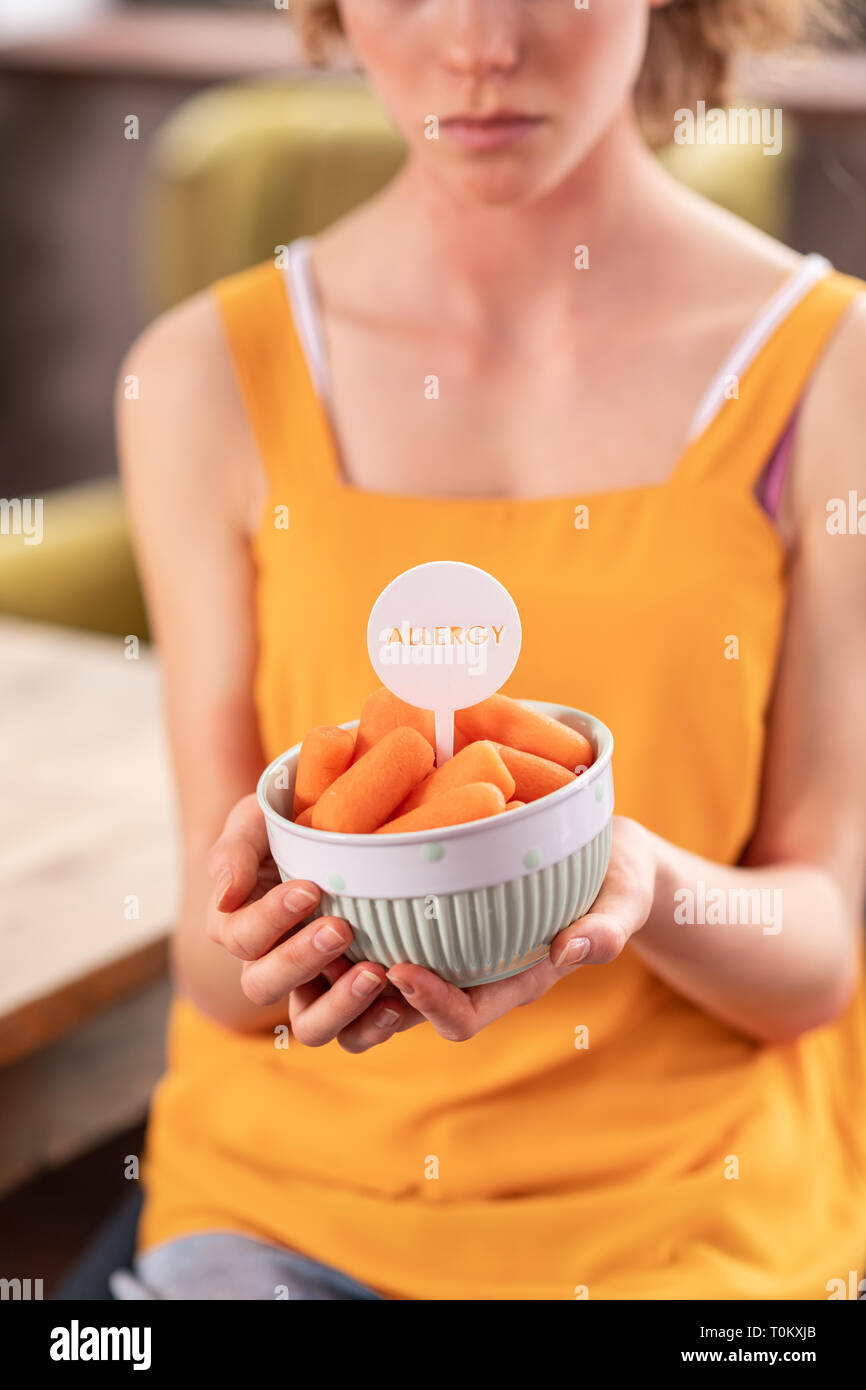 Unhappy skinny girl presenting bowl full of carrots Stock Photo