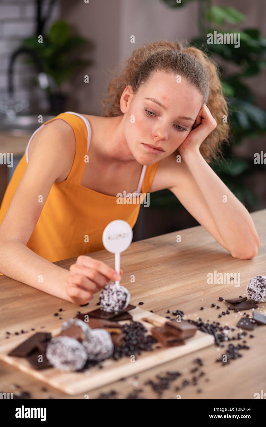 Woman in bright outfit leaning on wooden table covered with chocolate Stock Photo